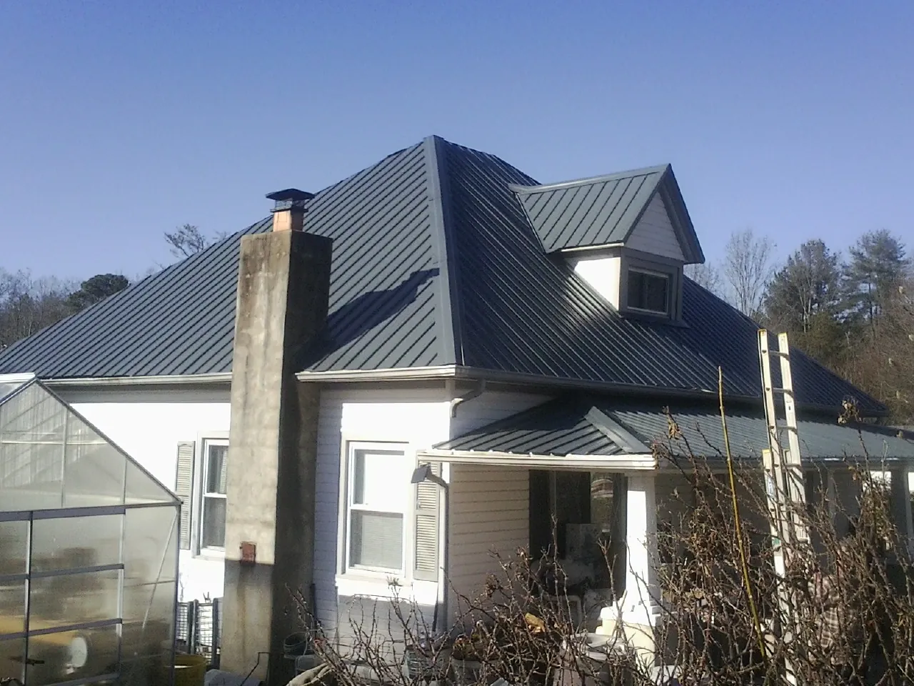Dark blue standing seam metal roof on a white farmhouse with dormer — Slate & Tile Roof Repair by Roofing Brothers in Laverne