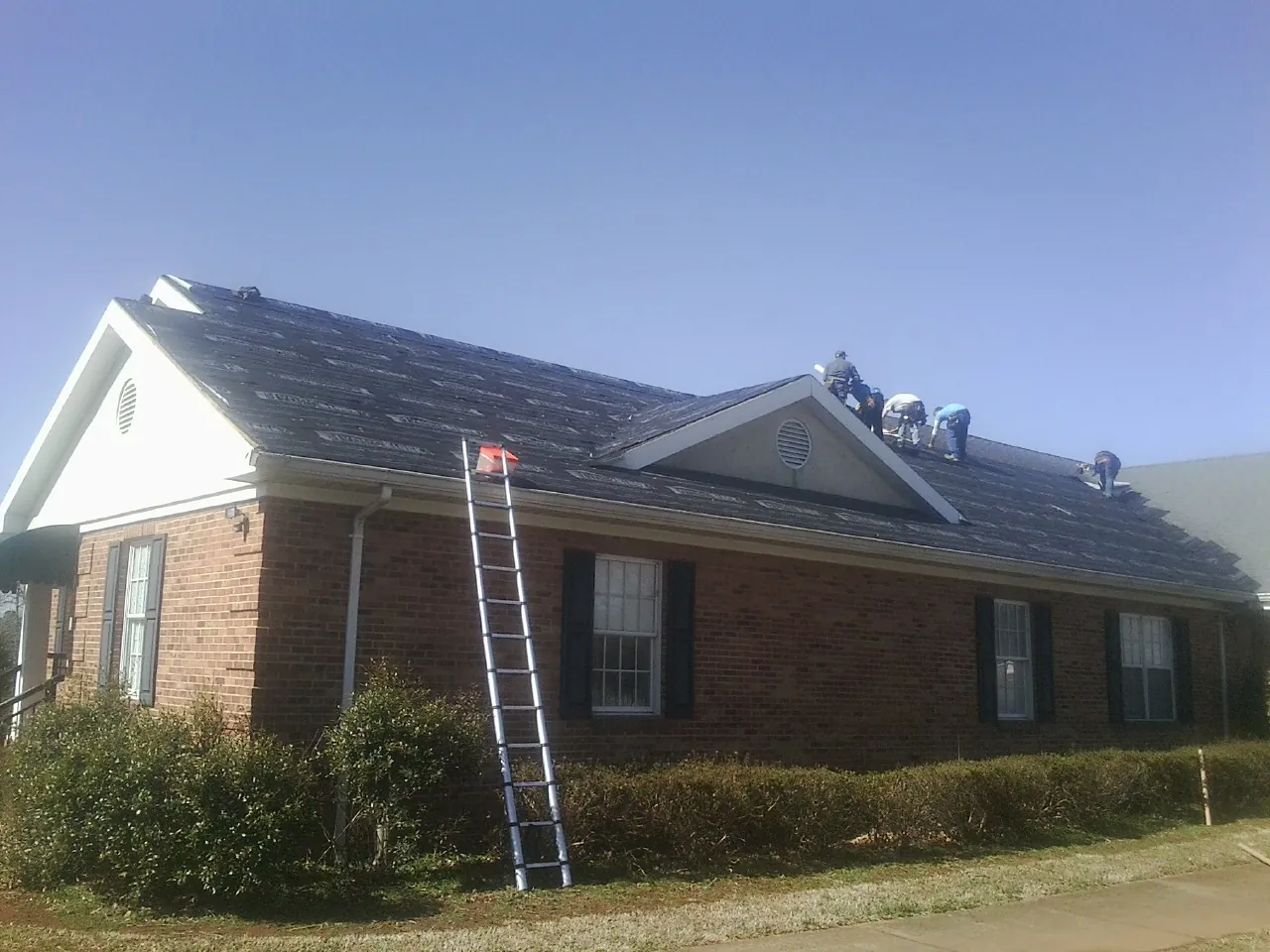 Crew tearing shingles off a brick ranch roof with a ladder set — Emergency Roof Repair work by our crew in Laverne