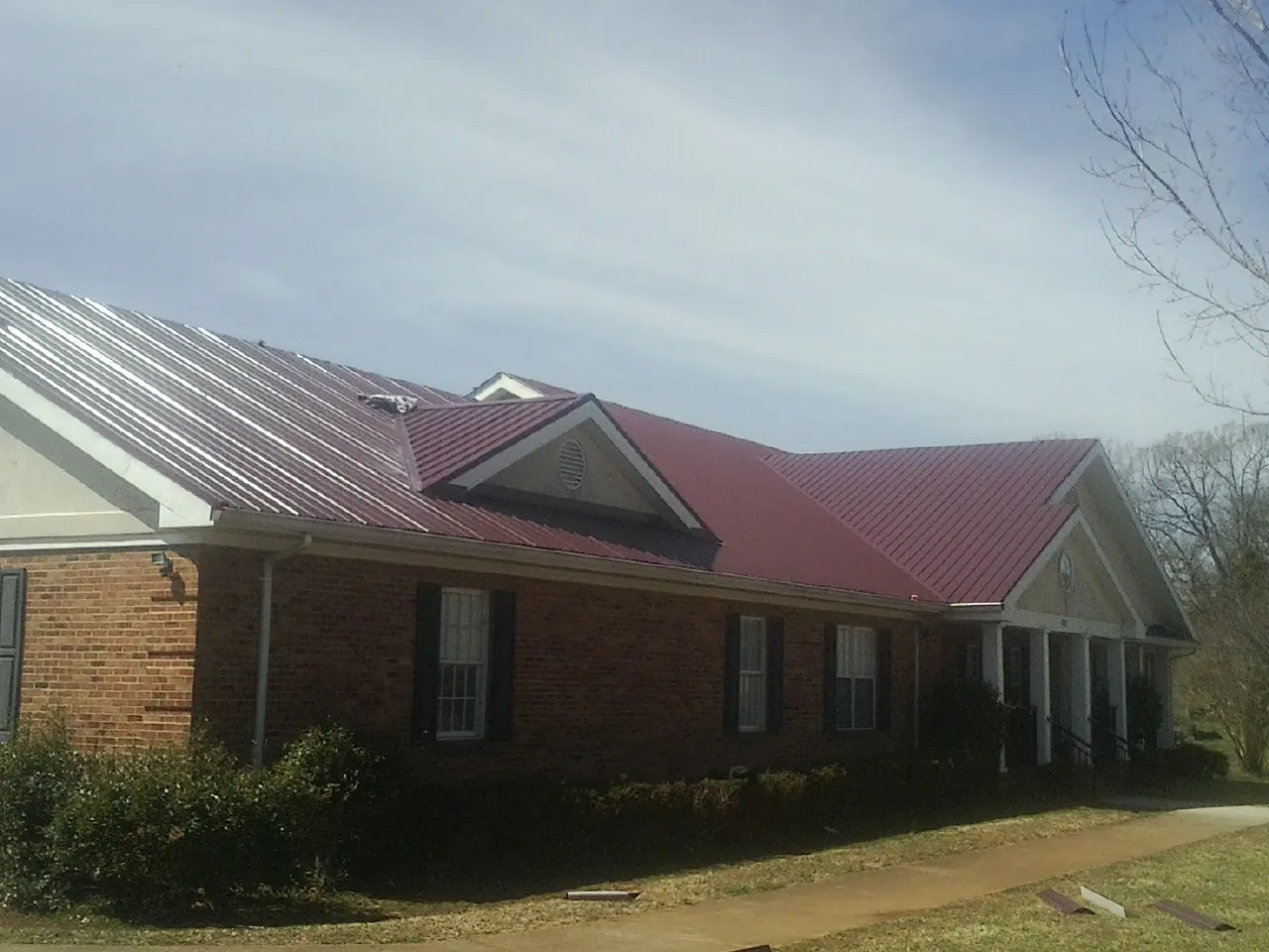 Red metal roof with gabled entries on a long brick building, from a Hail Damage Roof Repair job in Laverne