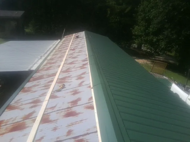 Old rusted panels beside newly installed green metal roofing — Wind Damage Roof Repair by Roofing Brothers in Laverne
