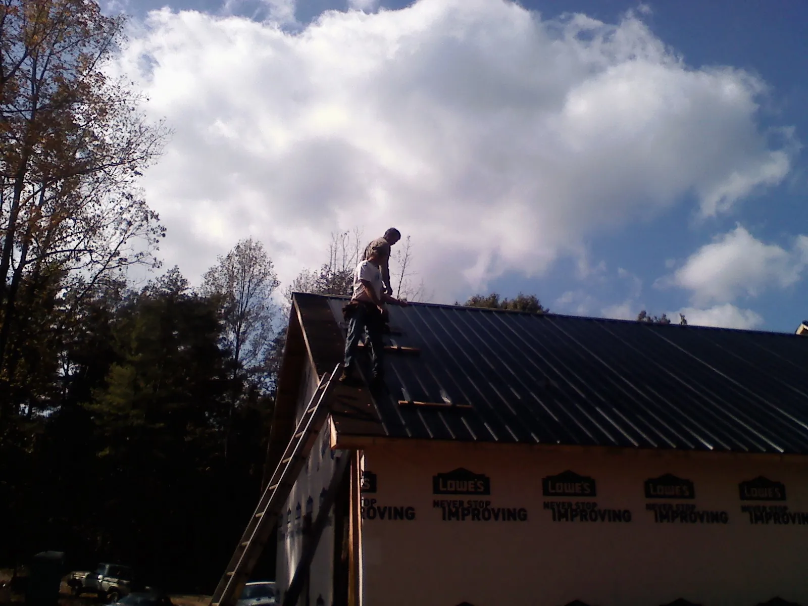 Roofer fastening dark metal panels high against a cloudy sky, from a Roof Inspection job in Laverne