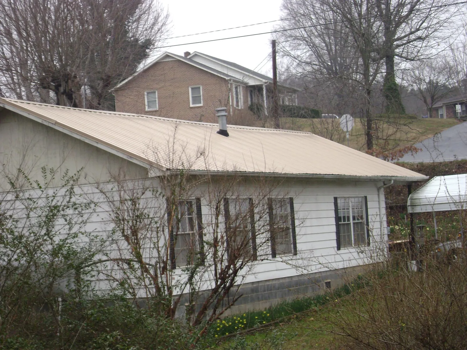 Tan metal roof on a white sided house set into a hillside — Commercial Roofing by Roofing Brothers in Laverne